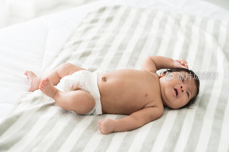 新生婴儿在白色的床上盖着毯子睡觉时啼哭。亚洲新生儿啼哭