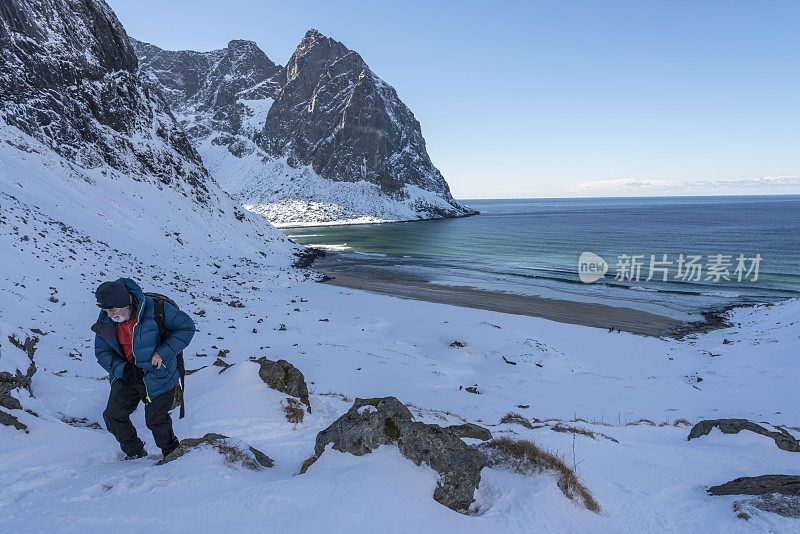 罗弗敦莫斯科索亚，一名男子在冬天爬上Kvalvika海滩上方的山丘