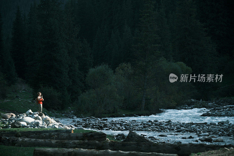 女游客在山河岸边徒步旅行并拍摄自己的视频