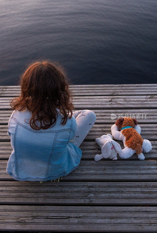 一个白人女孩，一个8岁的孩子，坐在木码头上看着湖面。