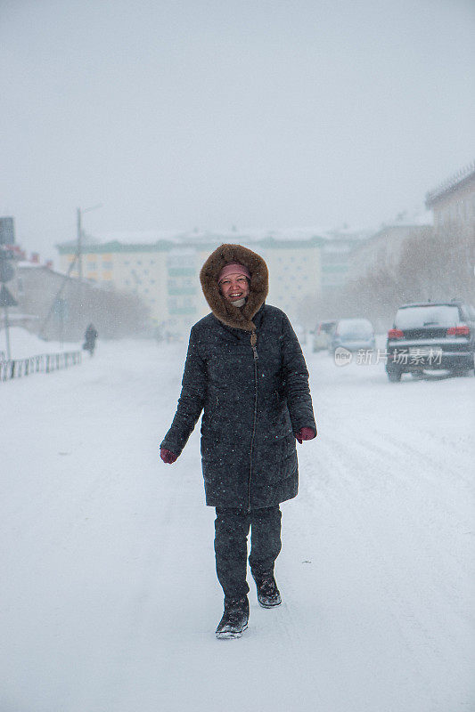 冬天来了，大暴雪来了。道路上有大雪，能见度低。妇女在危险的天气里缓慢而艰难地行走。大自然的大灾难。城市人的生活理念是暴风雪。