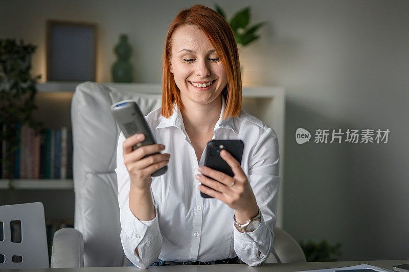 一位女企业家手持手机和遥控器在办公室调节空调，运用科技理念