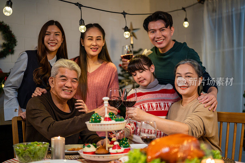亚洲家庭在家里一起庆祝圣诞派对的照片。迷人的父母和亲戚们在家里的餐桌上吃着感恩节大餐，庆祝圣诞前夜的节日。