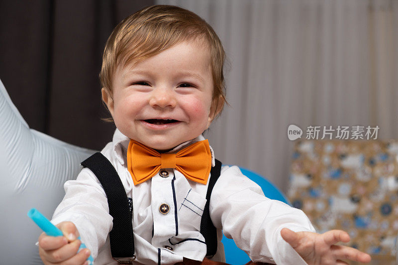 一个一岁的红发男孩的肖像，穿着衬衫，打着领结，穿着背带裤