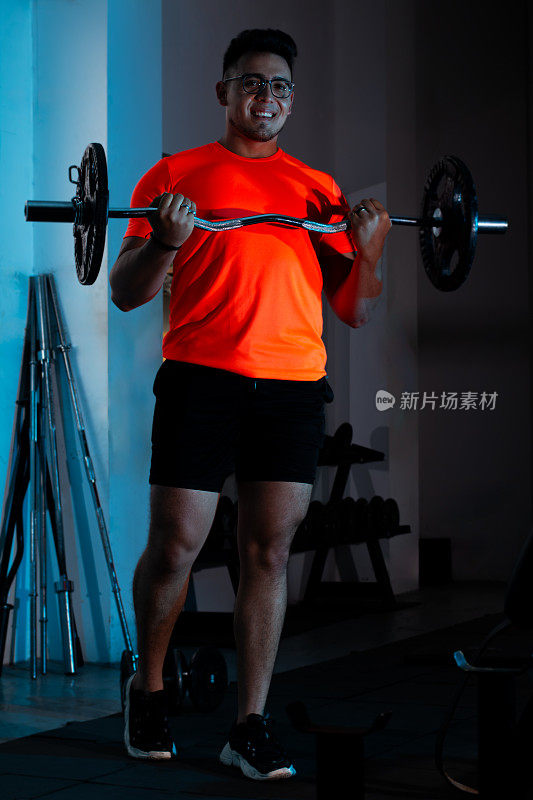 生活方式:穿着橙色衬衫的微笑年轻人举重，锻炼肱二头肌