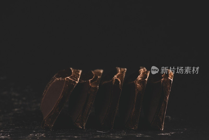 破碎的黑巧克力块堆叠在黑色背景上