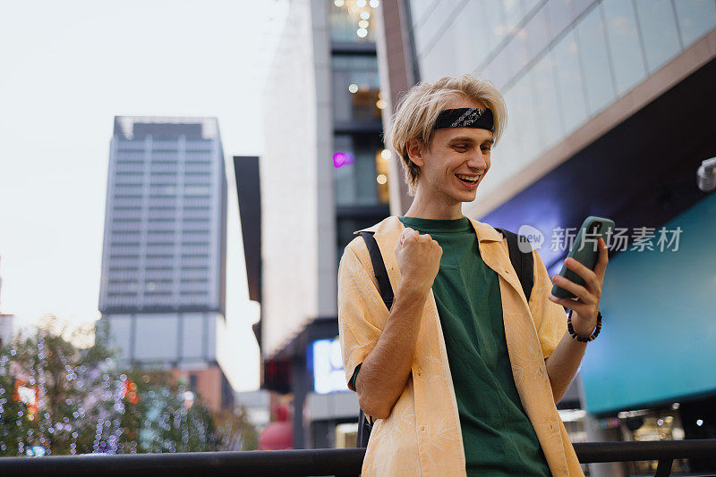 快乐的男学生在城市里通过手机阅读好消息。