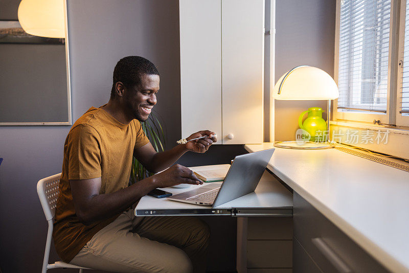 非裔美国人在家里一边吃零食一边用笔记本电脑工作