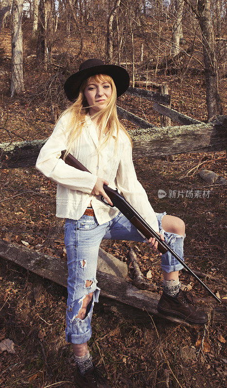 年轻的金发女人拿着枪站在树林里