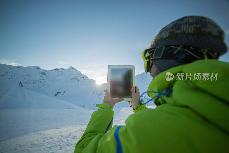 一名男子在雪山上用平板电脑拍照