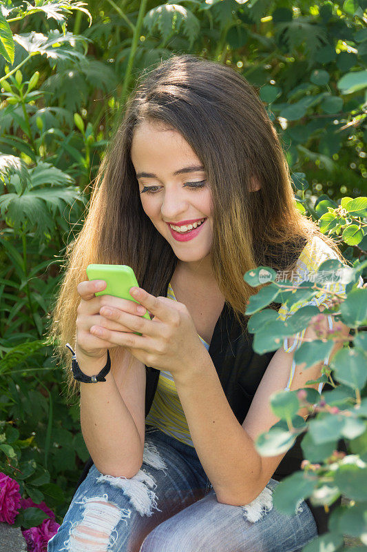少女在花园里，笑着手机短信。
