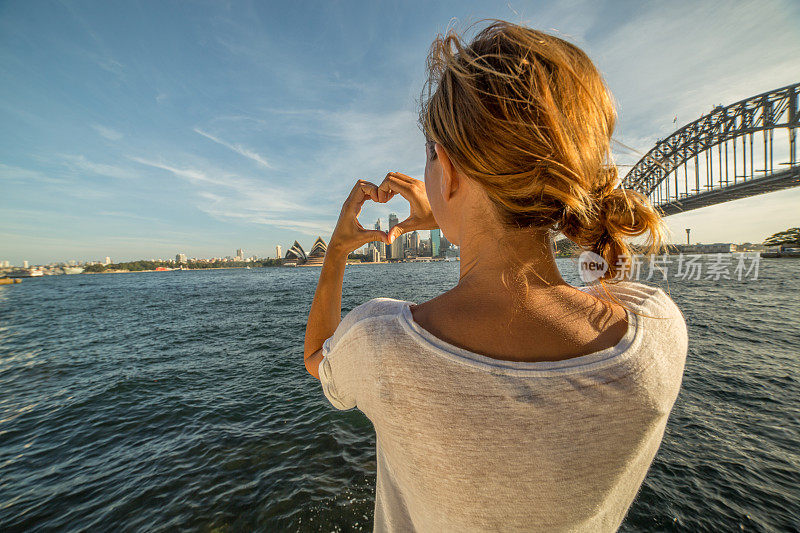 一个年轻的女人在悉尼的地平线上做心形的指架