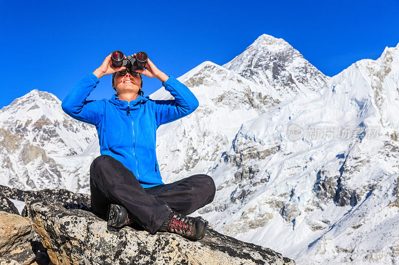 一个女人用双筒望远镜看，背景是珠穆朗玛峰