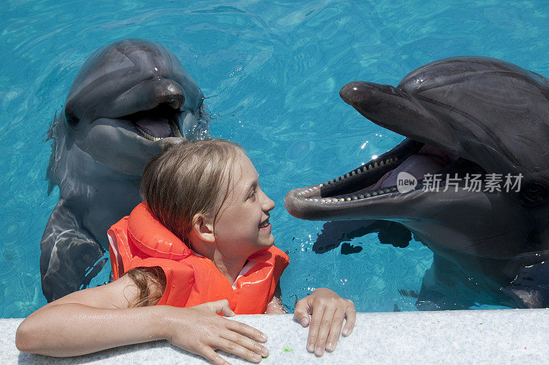 快乐的小女孩和两只海豚在游泳池里笑。