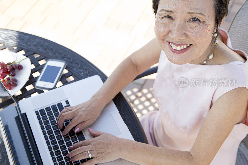 退休的亚洲资深女性在笔记本电脑上微笑