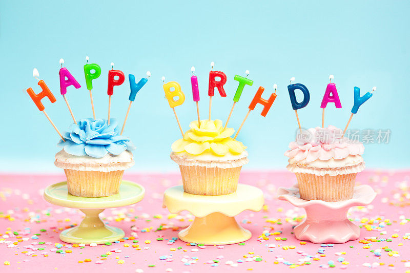 三个生日纸杯蛋糕，粉红背景上有蜡烛和五彩纸屑
