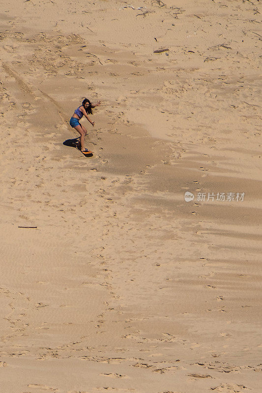 十几岁的女孩用沙板冲浪板从沙丘上高速下降