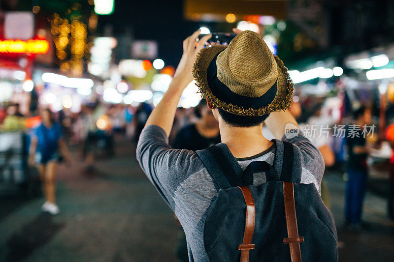 年轻的亚洲旅行者在夜晚的街道上用手机拍照