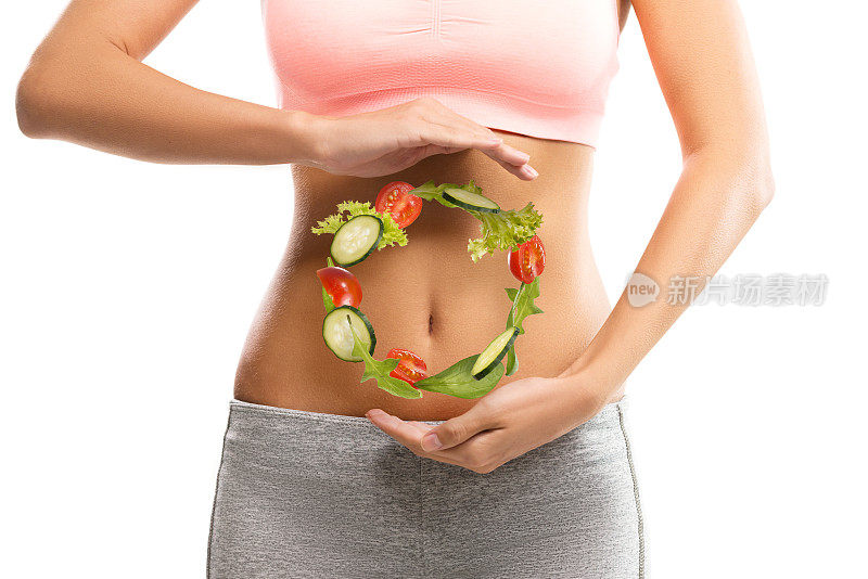身材匀称的年轻女子在腹部举着用蔬菜做成的圆圈