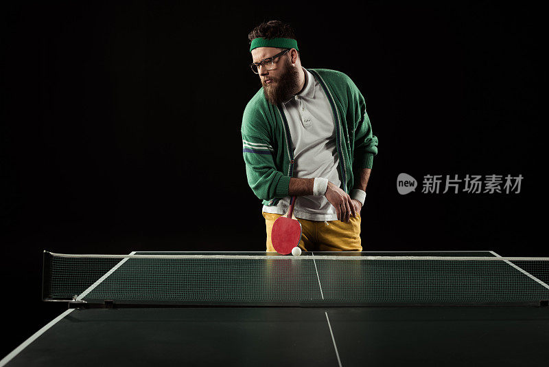 长着胡子的网球运动员靠在球拍上，孤立地靠在黑色的网球桌上