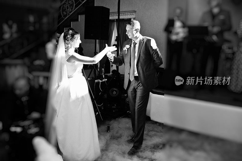 新婚夫妇在他们的婚礼上以浓重的烟雾和彩灯为背景跳舞。黑白照片。