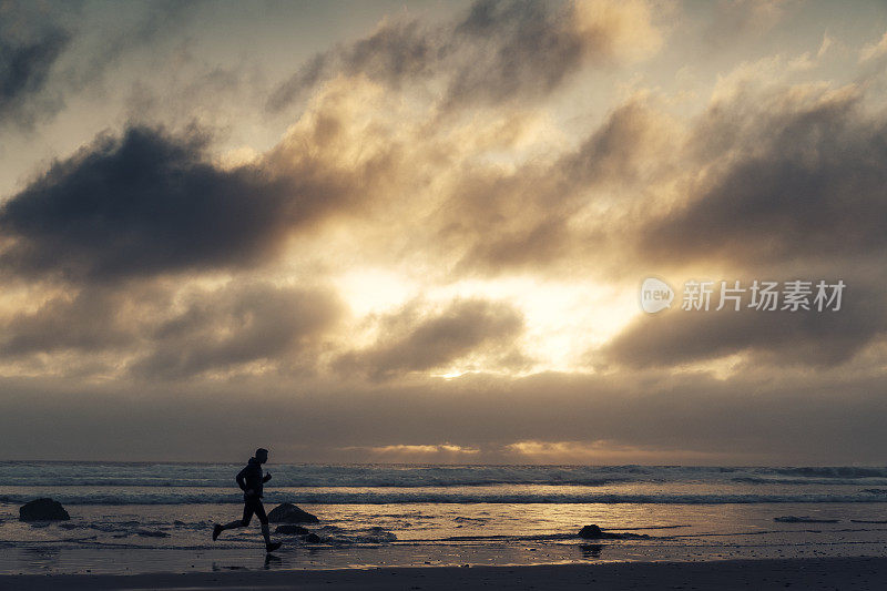 一个人的剪影沿着海滩跑在日落附近。