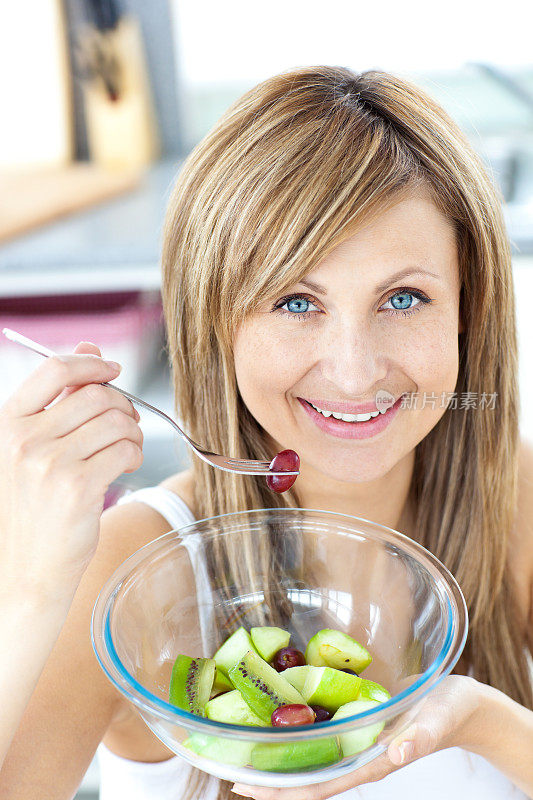 一个光彩照人的女人在厨房吃水果沙拉的肖像