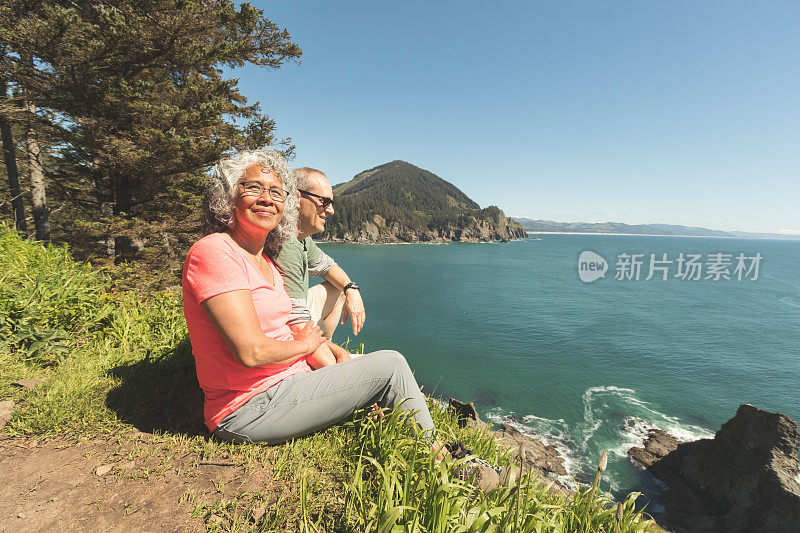 一对老年夫妇坐在俯瞰海洋的草崖上