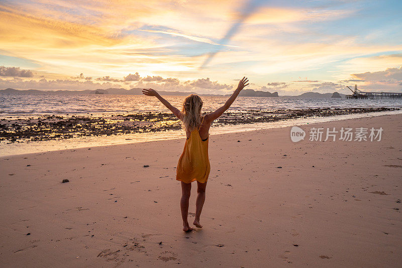 年轻女子走在海滩上伸开双臂享受热带气候异国度假。旅游目的地自由的人好奇的概念自然