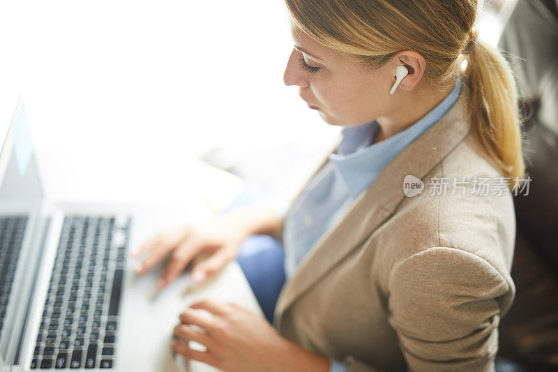 一个非常忙碌的女人戴着无线耳机在工作场所用笔记本电脑听音乐