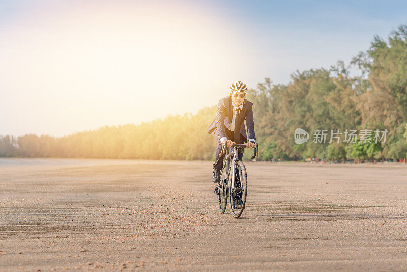 年轻的亚洲商人骑自行车放松海滩日落