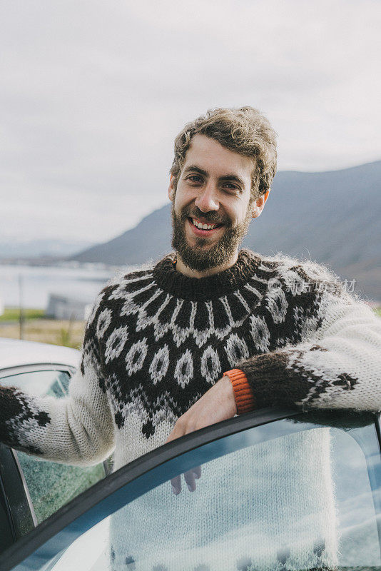 在冰岛，一个穿着冰岛毛衣的男人站在汽车旁边