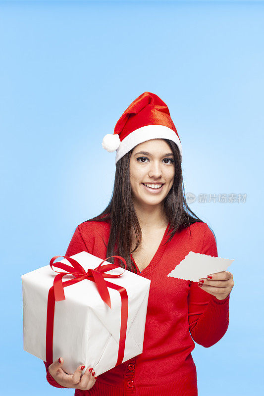快乐的女人戴着圣诞帽，拿着圣诞礼物，读着贺卡。