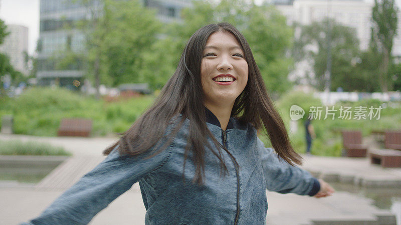 快乐的亚洲女人在公园跳舞。背景中的城市天际线