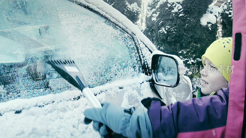 女司机刮着白雪覆盖的车窗