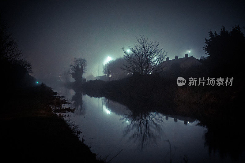 晚上雾气蒙蒙的运河，阴森恐怖的气氛，平静的运河水域和远处的房子