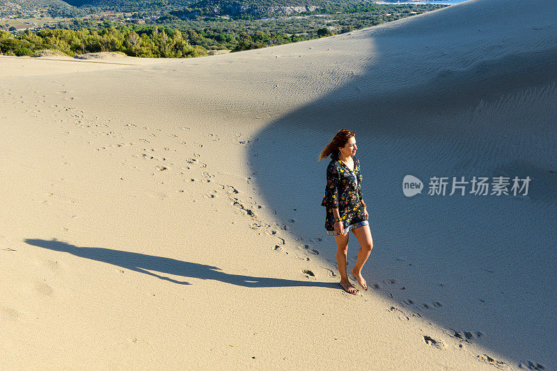 一个年轻漂亮的女人走在沙丘上。