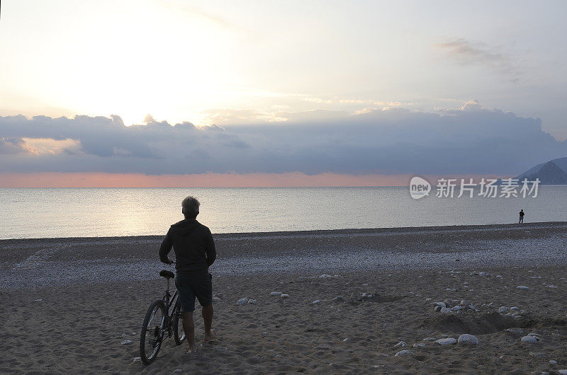 成熟的男人骑着自行车在日出的海滩上放松