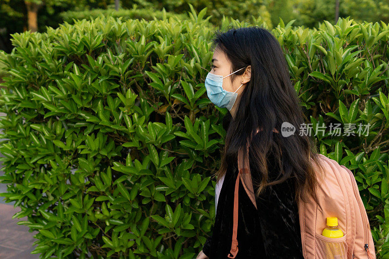 亚洲女学生背包戴防护医疗口罩。在冠状病毒关闭后，的学校将重新开学。
