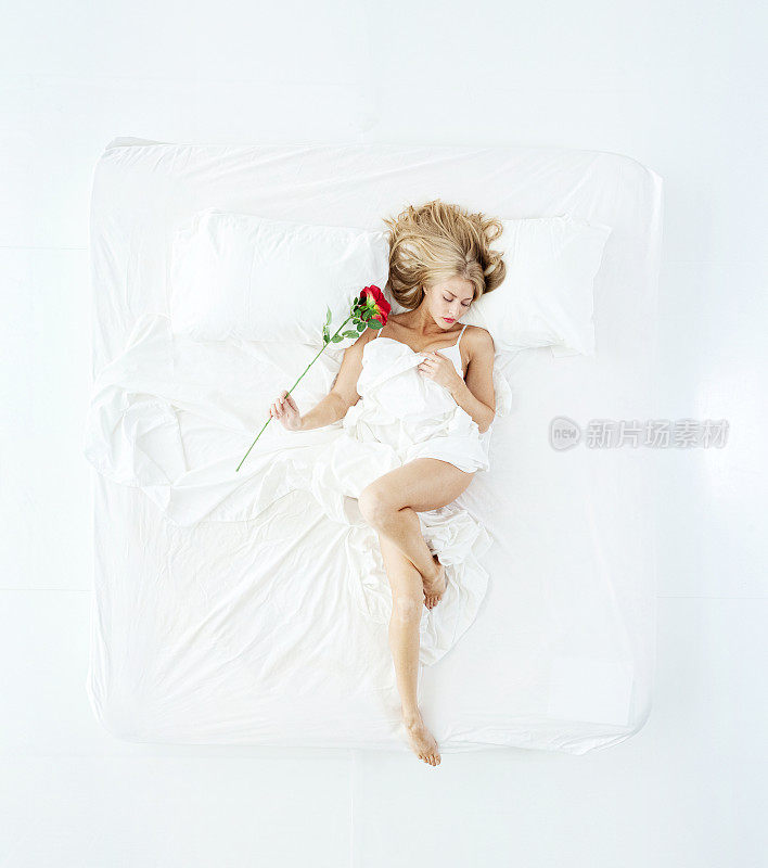 白种人年轻女性睡在白色背景的卧室里，穿着内衣和拿着玫瑰花