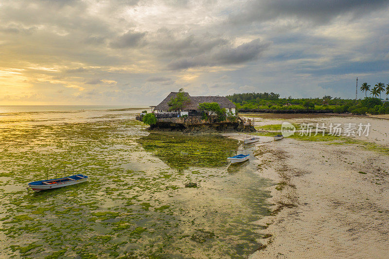 日落时分热带海滩上的房子和船。坦桑尼亚桑给巴尔岛上的房子