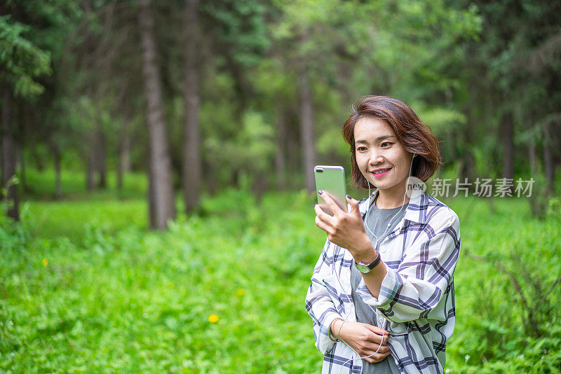 年轻的亚洲女子在森林里戴着耳机听音乐