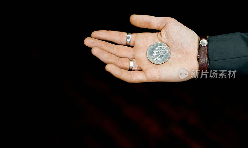 一枚硬币在一名男子的手掌上，背景为黑色的局部光