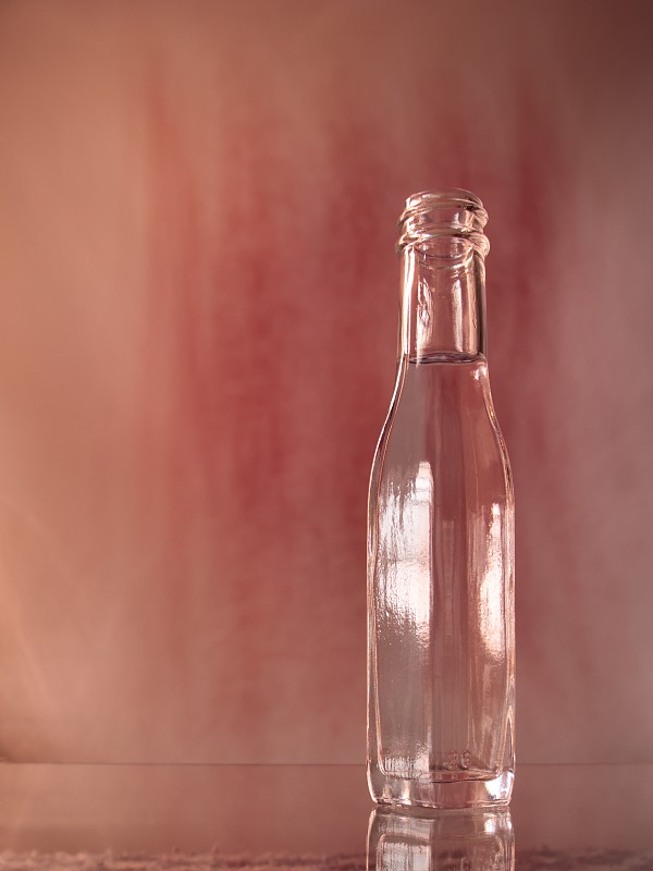 #肖像:一个装满无色液体的透明玻璃瓶，排列在一个闪亮的表面上，背景模糊染成红色。