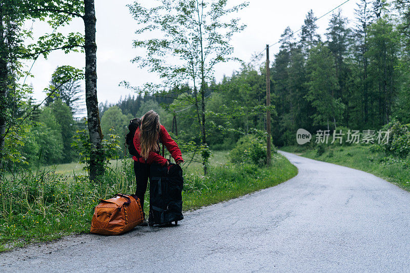 年轻女子背包客在雨中等待在路边与行李