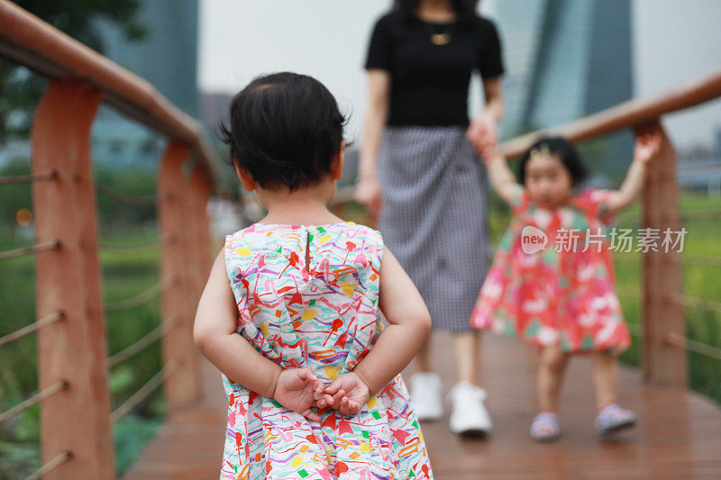 一个中国女孩双手合十，背对着她，她的姐姐和妈妈在后面