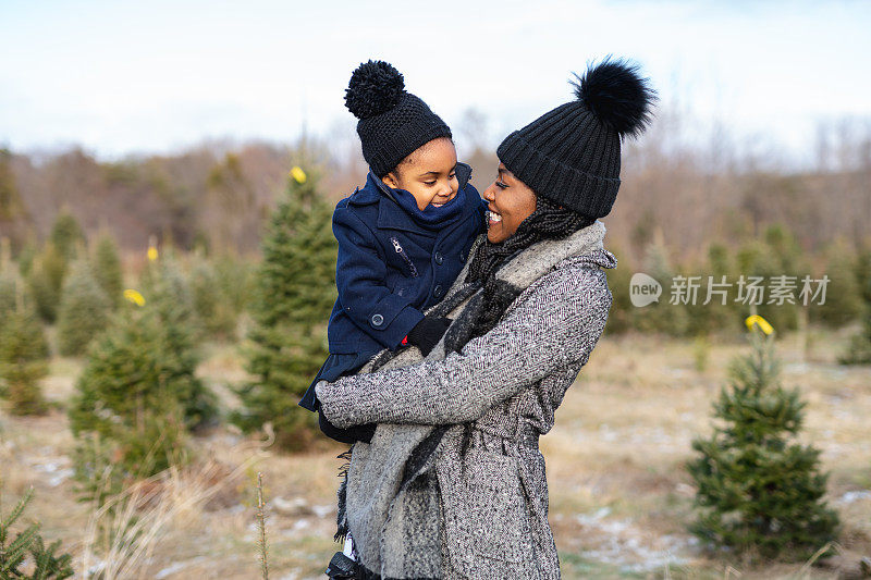 在圣诞树农场，一位美丽的母亲拥抱着她的小女儿