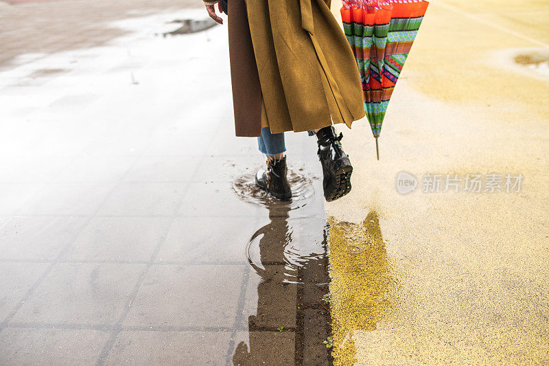 后视图，不认识的女人在大衣走过水坑在雨天在城市