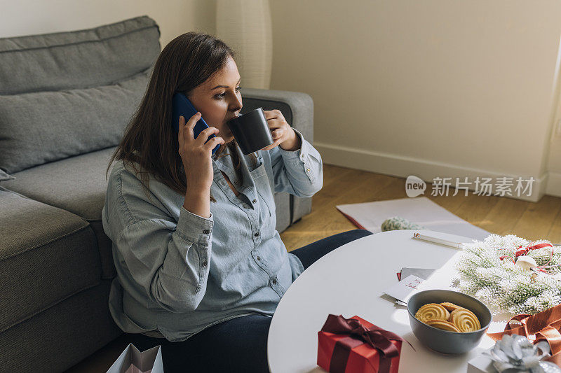 在圣诞节的早晨，美丽的大码女人在打电话，享受一杯咖啡