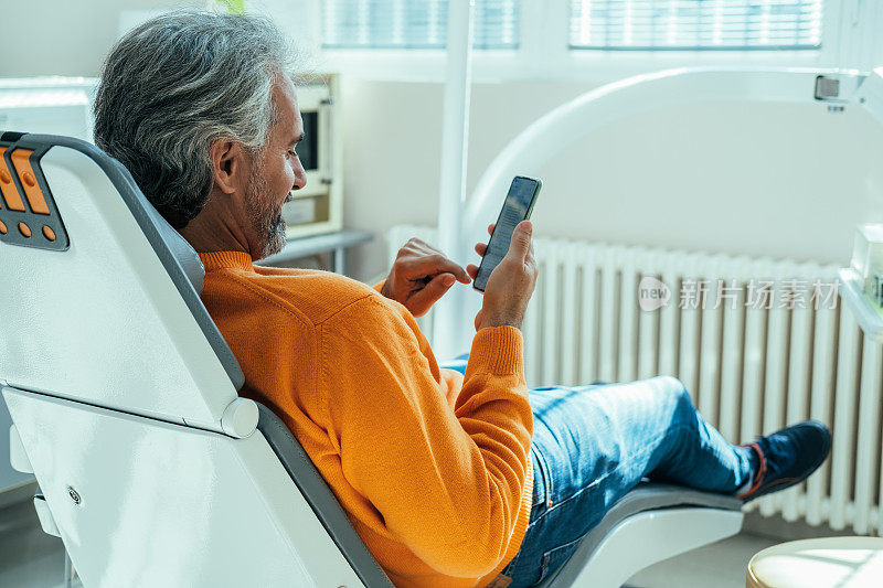微笑的成熟男人坐在牙医的椅子上用手机